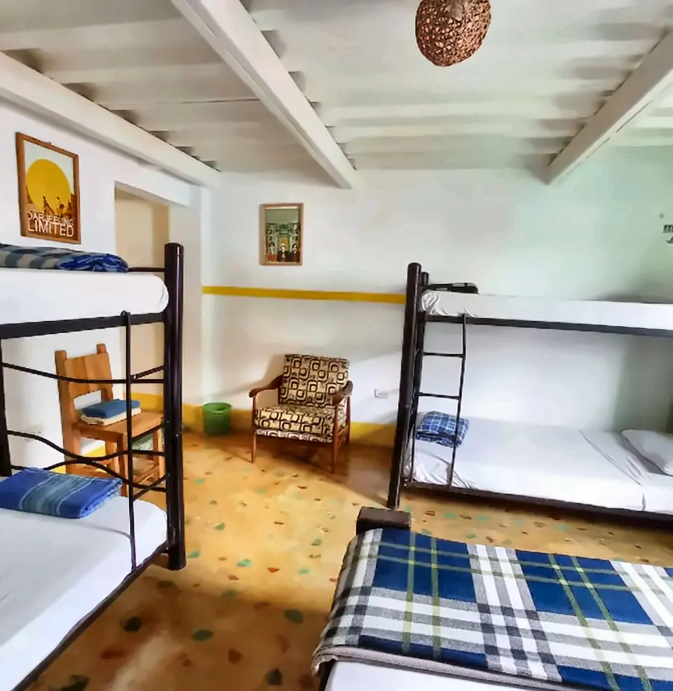 Dormitorio luminoso con dos literas de metal, una butaca, mantas a cuadros azules y piso de baldosa