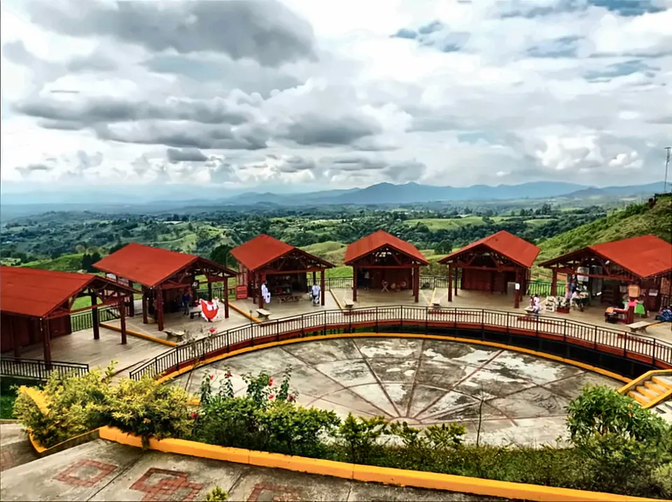 Panorámica desde el Mirador Colina Iluminada: kioscos de techo rojo en semicírculo y colinas verdes hasta el horizonte