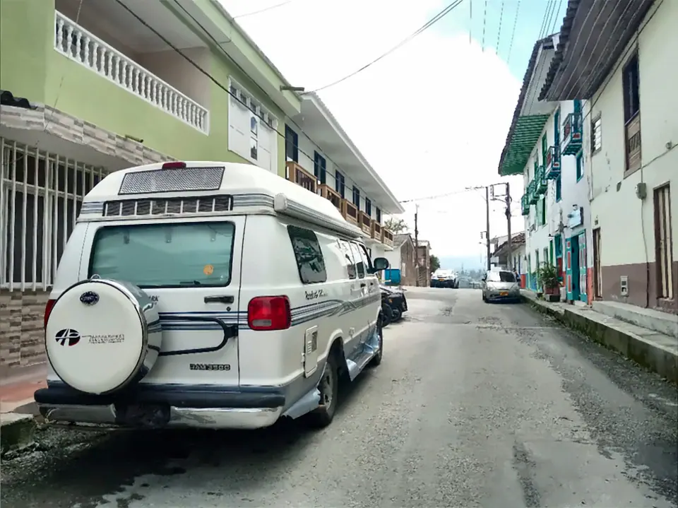 Una camioneta camper blanca estacionada en una calle de Filandia con casas de balcones de colores